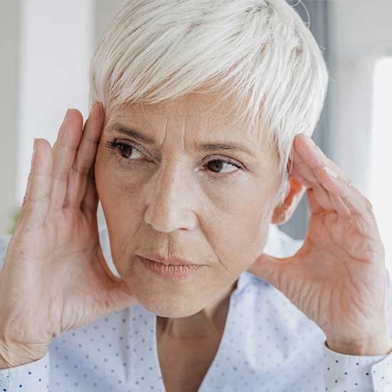 Frau greift sich mit beiden Händen an den Kopf, wegen des störenden Ohrgeräuschs. 